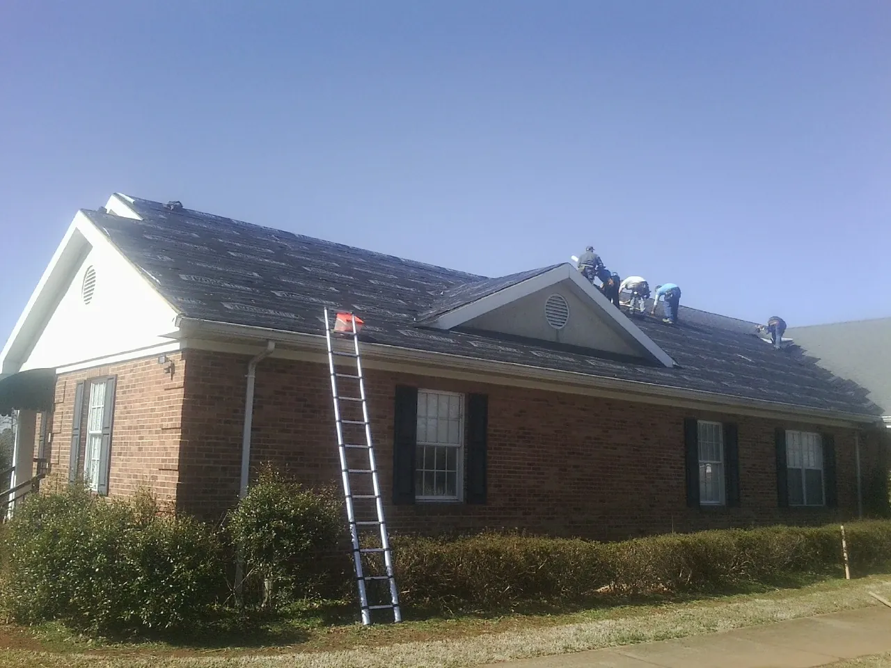 Crew tearing shingles off a brick ranch roof with a ladder set — Metal Roof Repair work by our crew in Marietta